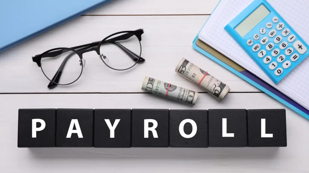 Calculator, cash, and glasses on payroll document – payroll outsourcing made easy