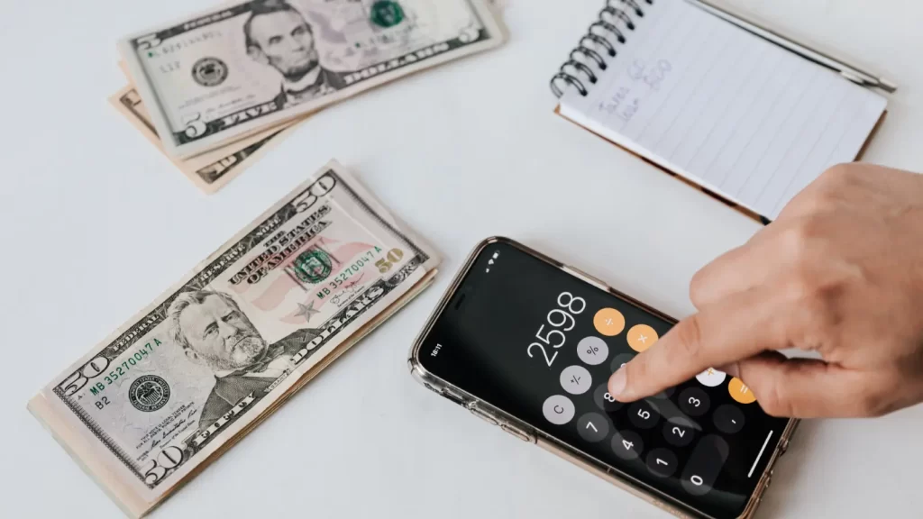 Payroll outsourcing planning with fifty dollar bills, phone calculator, and notebook on desk